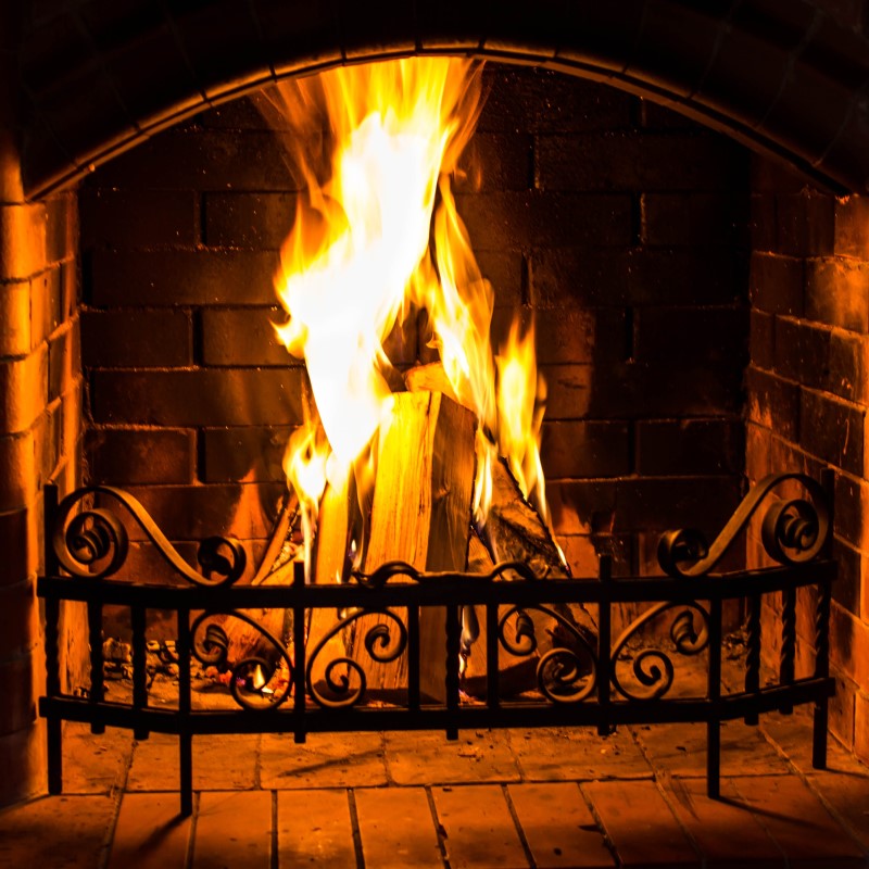 Roaring fire behind a fireplace grate with wood buring