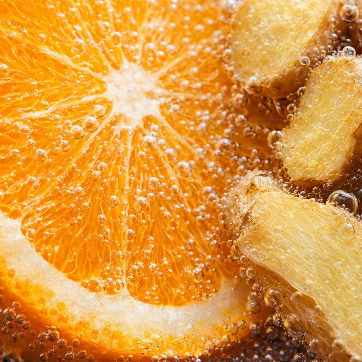 A close-up of a bright orange slice with ginger root pieces bubbling in a carbonated liquid, showing detailed citrus segments, bubbles, and warm golden ginger tones. To depict the smell of Orange Ginger Fizz fragrance oil.