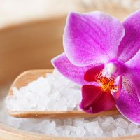Wooden spoon with white bath sea salts and a pink orchid flower on a wooden surface