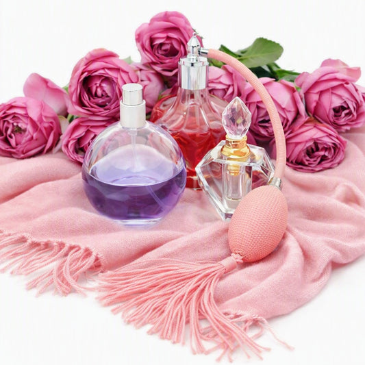 Cashmere Fragrance Oil depicted by a pink cashmere scarf with pink roses and bottles of perfume on the top.