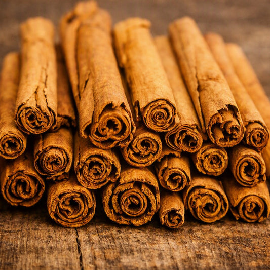 A close-up pile of whole cinnamon sticks with curled ends, arranged on a rustic wooden surface that gives the idea of the Cinnamon Stick Fragrance Oil.