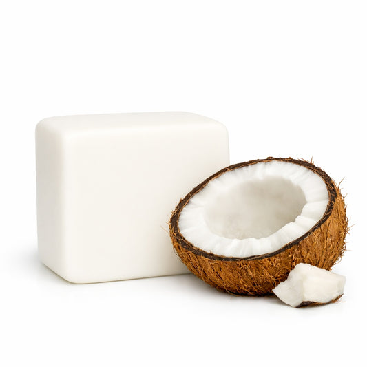Block of white cocoa butter melt and pour soap base next to a halved coconut on a white background