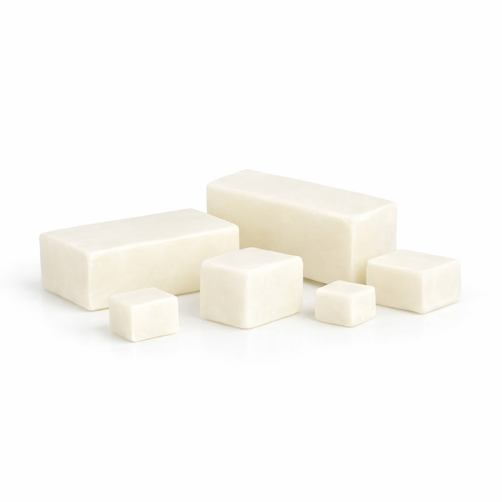 Six creamy white cocoa‑butter melt and pour soap blocks arranged simply on a white surface. Two larger rectangular pieces sit behind four smaller cubes, all with smooth matte texture and soft shadows under even lighting. Each piece could be used as a sample.