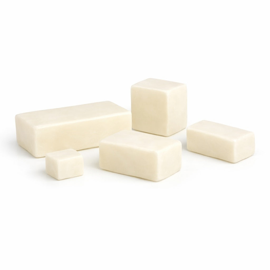 Five creamy white soap base blocks in assorted sizes arranged on a white surface, shown as a goat milk sample.