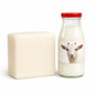 Block of goat milk soap base next to a glass bottle of goat’s milk with a goat on the label.