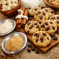 Oatmeal cookie bars with raisins arranged on a wooden board with cinnamon sticks, bowls of sugar, and a white pitcher on a burlap surface. Depicts the scent Grandma's Kitchen Fragrance Oil