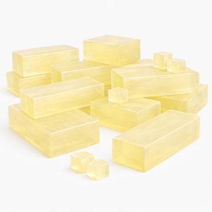 A collection of translucent honey melt and pour soap blocks arranged on a white background. The blocks vary in size, including larger rectangular bars and smaller cubes, all with a warm golden-yellow color and smooth, glossy surfaces. The pieces are grouped loosely together, showing their clarity.