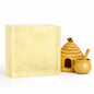   
A large translucent honey melt and pour soap block displayed beside a small woven beehive, a ceramic honey pot with a honey dipper, and a decorative bee perched on the hive. The soap has a warm golden color with smooth, glossy surfaces, and the scene is arranged on a bright white background to emphasize the honey theme and natural ingredients.