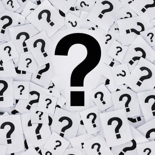 A central large black question mark on a white card, surrounded by many scattered white cards, each printed with a black question mark. Gives the idea of It's A Mystery Fragrance Oil scent.
