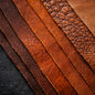A close-up arrangement of multiple leather strips in different shades and textures, including smooth, pebbled, and grain finishes in warm brown, tan, and reddish-brown tones. To get the feel for leather fragrance oil.