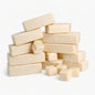 A loose stack of thirteen creamy oatmeal melt and pour soap base bars with a few small cubes scattered nearby, all set against a clean white background. The bars and cubes have smooth surfaces with visible golden specks, highlighting their natural oatmeal texture.