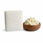 A square block of white shea melt and pour soap base sits on a clean white background beside a small wooden bowl filled with creamy shea butter. The soap has smooth, slightly rounded edges and a matte finish, while the shea butter appears soft and natural with a rich, off‑white color.