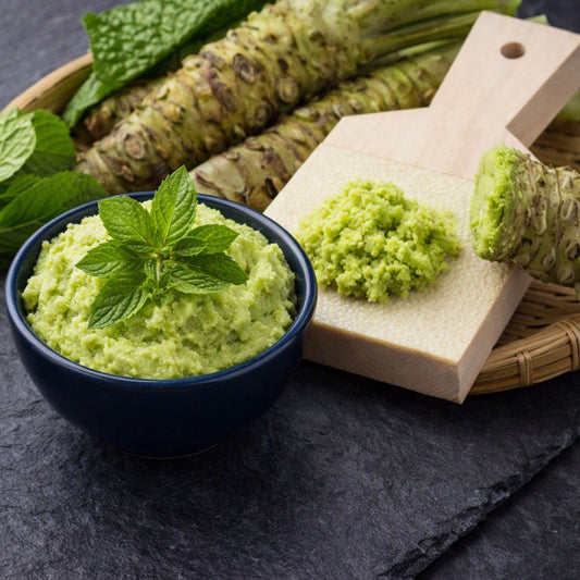 Fresh green wasabi mash in a dark blue bowl with mint leaves, alongside a wooden cutting board holding a piece of wasabi and a scoop of mashed wasabi, set on a dark slate surface. Gives the feel for Wasabi Mint Fragrance Oil by Northstar.
