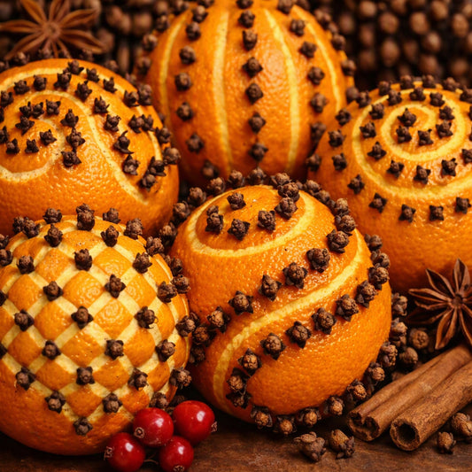 Several orange spheres decorated with cloves and star anise, arranged on a rustic wooden surface with cinnamon sticks and red berries. Looks like what Zanzibar Clove Fragrance Oil smells like.